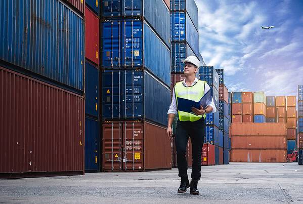 Logistics professional walking beside shipping containers at a cargo terminal